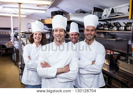 Group of happy chefs smiling at the camera in a kitchen wearing uniforms