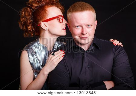 redhead couple. red-haired girl something seductively whispering in the ear of the red-haired man. Black background