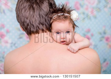 1 month little girl looks through a shoulder dad on a light background