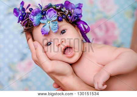 Portrait of a baby girl with a wreath of violet flowers on her head on a light background