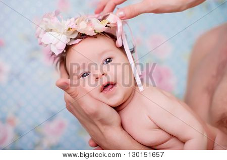 Portrait of a baby girl with a wreath of pink flowers on her head on a light background