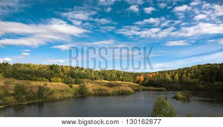 autumn landscape with a forest on the shore of the lake and the blue sky with clouds