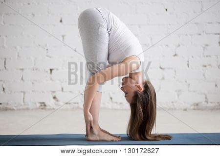Attractive Fit Young Woman Doing Standing Forward Bend Pose In White Loft