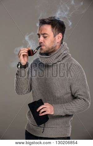 man lights a pipe with a match in the studio on a gray background
