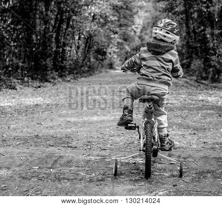 child riding a bicycle in the woods. Black and withe