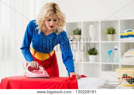 Pretty young superwoman ironing her red cape