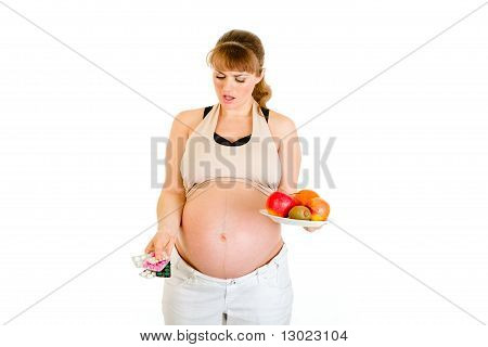 思いやりのある妊娠中の女性の丸薬と白で隔離の果物の間の選択を行う