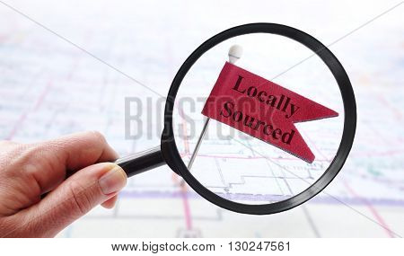 Hand holding a magnifying glass over Locally Sourced pin flag