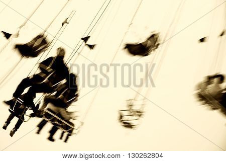 The abstract silhouettes of sitting visitors on a rotating swing ride.