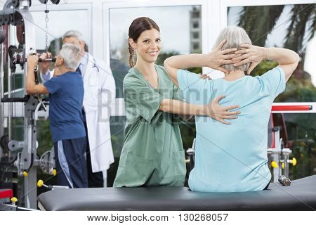 Female Nurse Assisting Senior Woman In Back Exercise