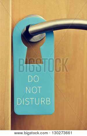 closeup of a blue door hanger with the text do not disturb hanging on the handle of a pinewood door