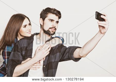 tehnology, internet, emotional  and people concept: Capturing happy moments together. Happy young loving couple making selfie and smiling while standing against white background.