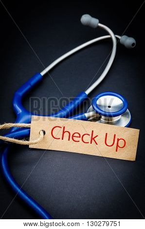 Check up word in paper tag with stethoscope on black background - health concept. Medical conceptual