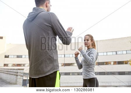 fitness, sport, people, exercising and martial arts concept - young woman with trainer working out self defense strike on city street