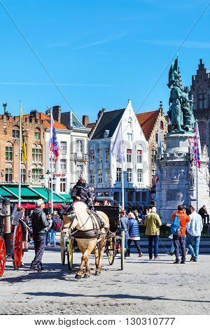 Bruges, Belgium - April 10, 2016: Market place or Grote Markt square with colorful traditional houses, fiaker, people in popular belgian destination
