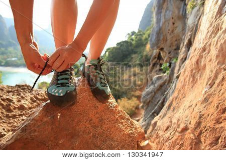 young woman rock climber tying shoelace at mountain rock