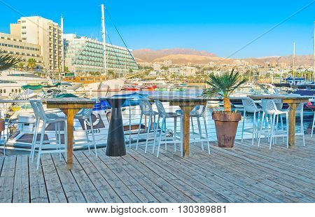 EILAT ISRAEL - FEBRUARY 23 2016: The cozy outdoor cafe on the wooden terrace in marina with the view on the white yachts on February 23 in Eilat.
