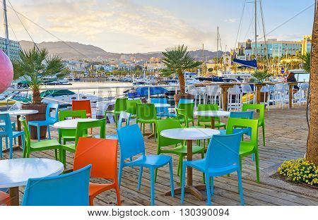 The scenic outdoor cafe in Lagoona of Eilat with the picturesque view on the moored yachts green palms and the mountains in the sunset lights Israel.