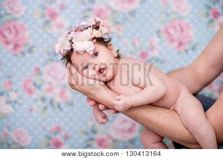 Portrait of a baby girl with a wreath of pink flowers on her head on a light background