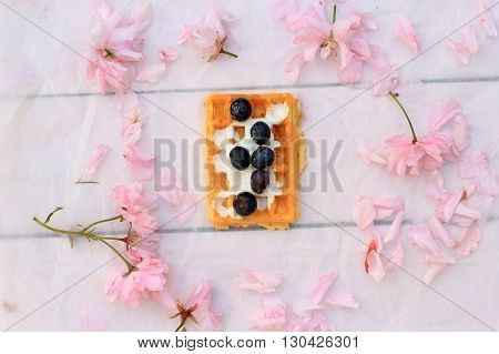 Freshly baked belgium waffles on romantic wooden taable with pink cherry flowers