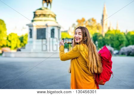 Young female tourist with back pack photographing with smart phone Austrian national hero monument on Hendel square.