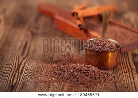 grated dark chocolate in copper measure pan on wooden background