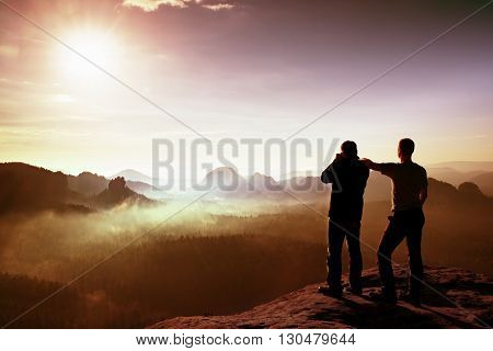 Two Friends. Hiker Thinking And Photo Enthusiast Takes Photos  Stay On Cliff. Dreamy Fogy Landscape,