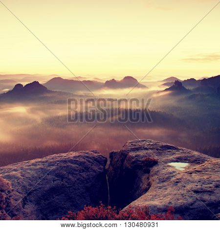 Fantastic dreamy sunrise on the top of the rocky mountain with the view into misty valley