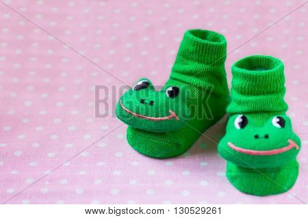 Pair of green child socks with frogs toys closeup on spotted pink background, selective focus