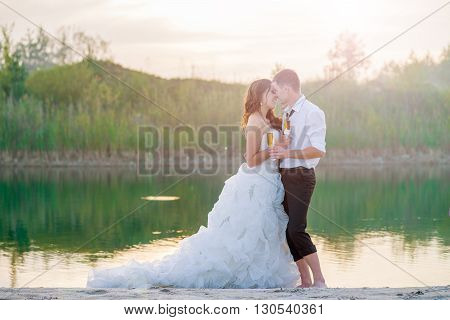 Romantic young and happy bride on the lake with a glass of wine at sunset. Horizontal