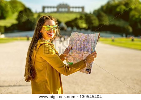 Young female tourist traveling with paper map in Schoenbrunn palace with Gloriette building on the background