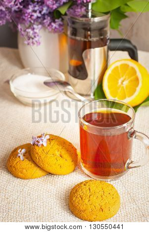 still-life with a cup of tea with lemon sugar oatmeal cookies vase of lilac on the linen cloth and a wooden surface in bright colors