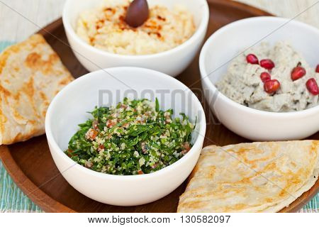 Assortment of dips: hummus, chickpea dip, tabbouleh salad, baba ganoush and flat bread, pita on a plate. Summer outdoor background