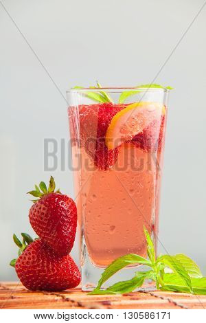 Glass of strawberry lemonade with pieces of strawberry, lemon and fresh mint. Closeup of mojito with beach on background. Fresh summer bright strawberry cocktail.