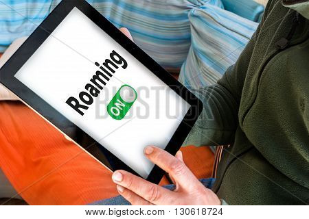 Hand holding black tablet with roaming on words on white screen (Turn on data roaming)