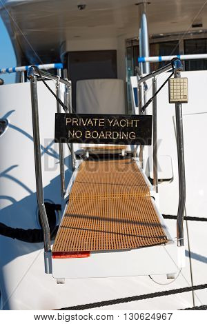 Black sign on a gangway of a luxury yacht with text Private yacht no boarding