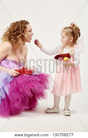 Lttle daughter holding box in shape of heart with cookies treats her mother with cookie.