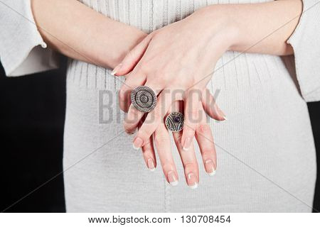 Female hands with signet rings on fingers over white knitted dress.