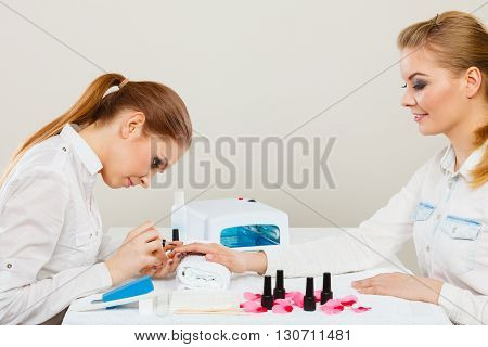 Relaxing time and wellness day concept. Blonde elegant woman visiting professional manicurist salon. Beautician makes perfect nails to client.