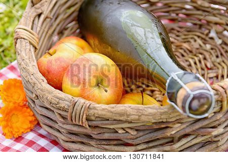 a bottle of cider with apples in a basket