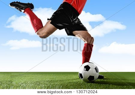 close up legs of football player in red socks and black shoes running and kicking the ball in free kick action playing outdoors on green grass pitch under a blue sky