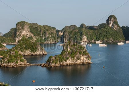 Distant View of the lush green covered limestone karsts formation on Ha Long Bay in Vietnam. The clear blue sky looks gorgeous. Tourist boats are seen sailing on the blue water.