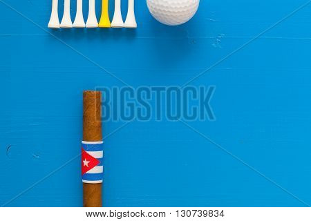 Detail of luxury Cuban cigars and golf equipments on the blue wooden desk