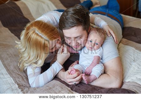 Beautiful happy couple and their baby relaxing in a bed together.