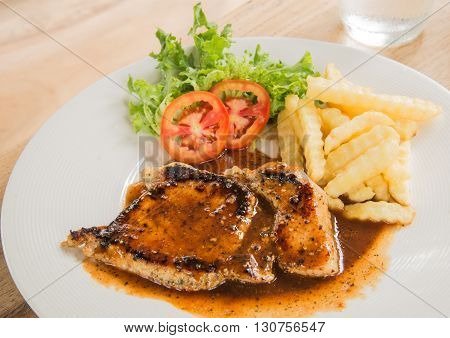 Pork steak in White plateGlass of waterFrench fries placed on wooden table.