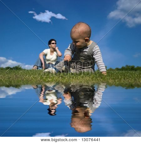 10 Monate altes Baby ist im Freien spielen, während seine Mutter im Hintergrund entspannend ist.
