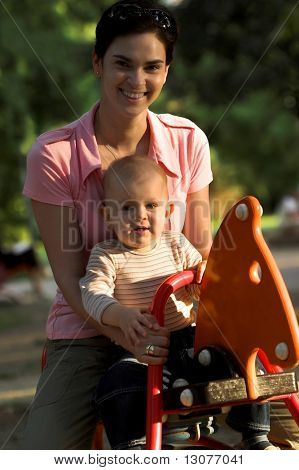 One year old baby is and his mother are swinging together on a cockhorse on the playground.