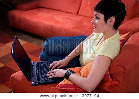 Junge Frau nutzt einen Laptop Computer ist ihr gemütliches Wohnzimmer.