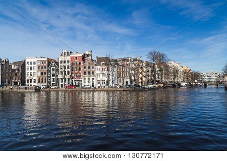 AMSTERDAM NETHERLANDS - 16TH FEBRUARY 2016: A view along canals in Amsterdam during the day. Buildings boats and people can be seen.