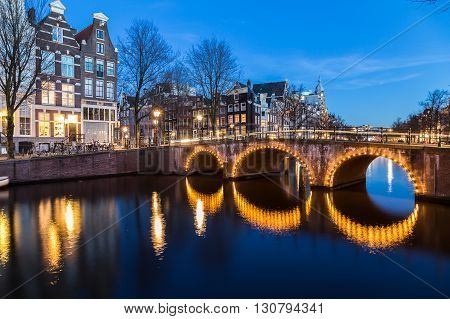 A view of the bridges at the Leidsegracht and Keizersgracht canals intersection in Amsterdam at dusk. Bikes and buildings can be seen.